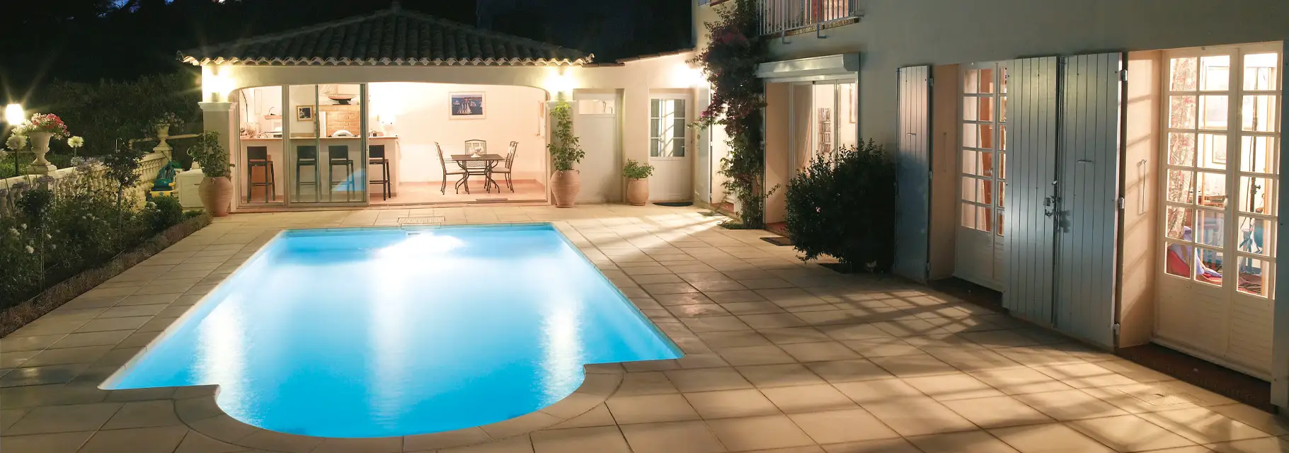 Beleuchteter Pool mit Terrasse und Garten am Abend